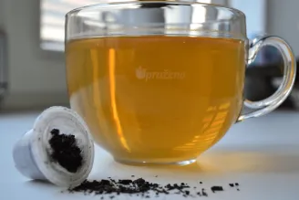 Skleněný šálek teplého nápoje a použitá kapsle na bílém stole