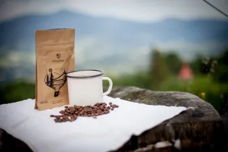 balík kávy kávová zrna a bílý šálek na bílé utěrce na dřevěném povrchu s venkovní krajinou v pozadí