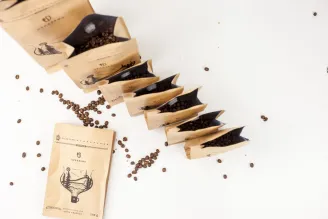 Různé balíčky kávy a zrnka rozmístěné po světlém stole