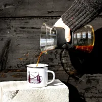 moka konvička nalévá kávu do bílého hrníčku s fialovým motivem mostu