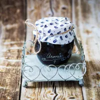 Tmavá skleněná lahev bylinného sirupu s látkovým víkem modrý květinový vzor a jutový provázek na kovovém stojánku na dřevěném stole