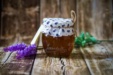 Skleněná dóza s hnědým bylinným sirupem Levandule látkové víčko s modrým vzorem a provázek vedle na dřevěném stole