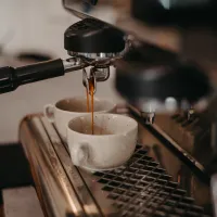 espresso kávovar s portafilterem kapající espresso nad dvěma bílými šálky