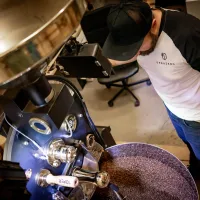 Pražená zrnková káva muž u pražicího stroje s miskou plnou pražených zrn