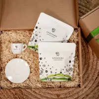 Balíček se dvěma bílými sáčky UPRÁZENO a bílým šálkem a podšálkem v kartonové krabici se slámou