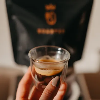 espresso crema ve skleničce s černým balením kávy v pozadí