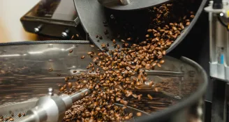 Pražená kávová zrna vycházejí z bubnového pražiče do kovového zásobníku