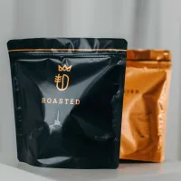 Zrnková káva dva pytlíky černý a oranžový s nápisem ROASTED v popředí