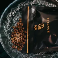 Roasted balení kávy černé barvy s oranžovým pruhem nápisem ROASTED vedle zrnkové kávy