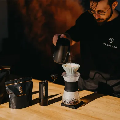 Pour over kávovar s papírovým filtrem nad skleněnou karafou na dřevěném stole černé balení ROASTED